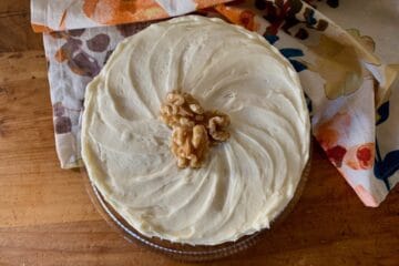 A Carrot Spice Cake, viewed from the top, covered in Cream Cheese Frosting and topped with several walnut halves.