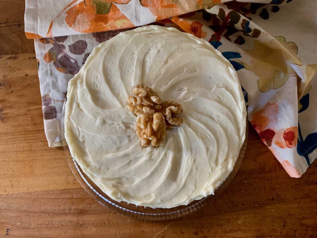 A Carrot Spice Cake, viewed from the top, covered in Cream Cheese Frosting and topped with several walnut halves.