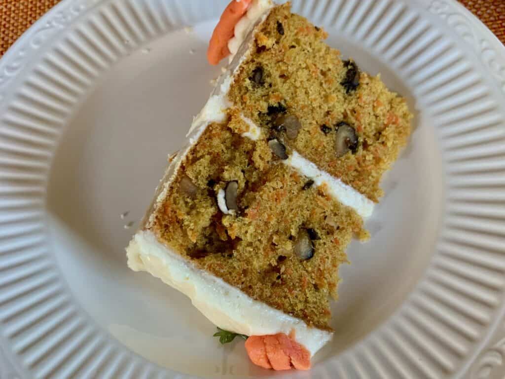 A slice of a layered Carrot Spice Cake iced with Cream Cheese Frosting and topped with Cream Cheese Carrots.