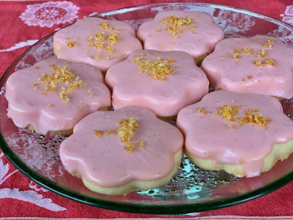Compari Iced Shortbread Cookies are topped with Golden Orange Sugar and arranged on a green glass cake stand. 