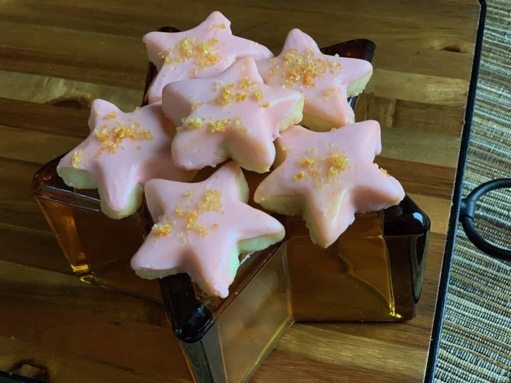 Star shaped Campari Shortbread Cookies are arranged on an amber glass star dish and wooden cutting board. 