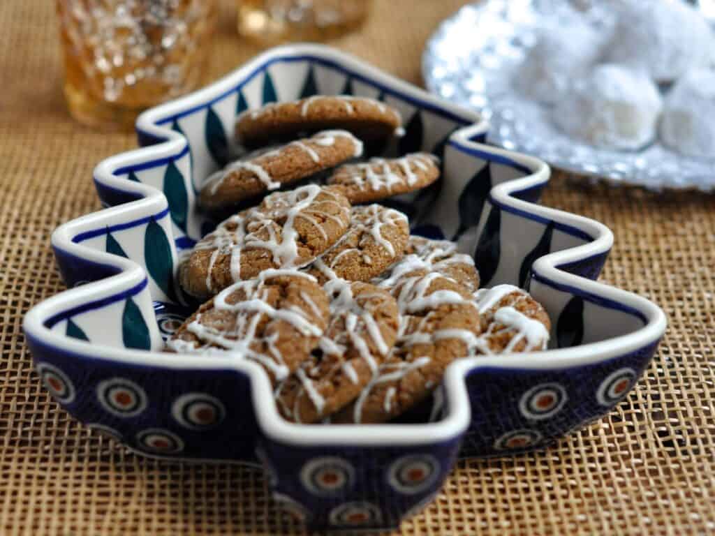 Spicy Molasses Crinkles drizzled with Icing are served in a Polish Pottery Christmas Tree Tray with Russian Teacakes and candles in the background.