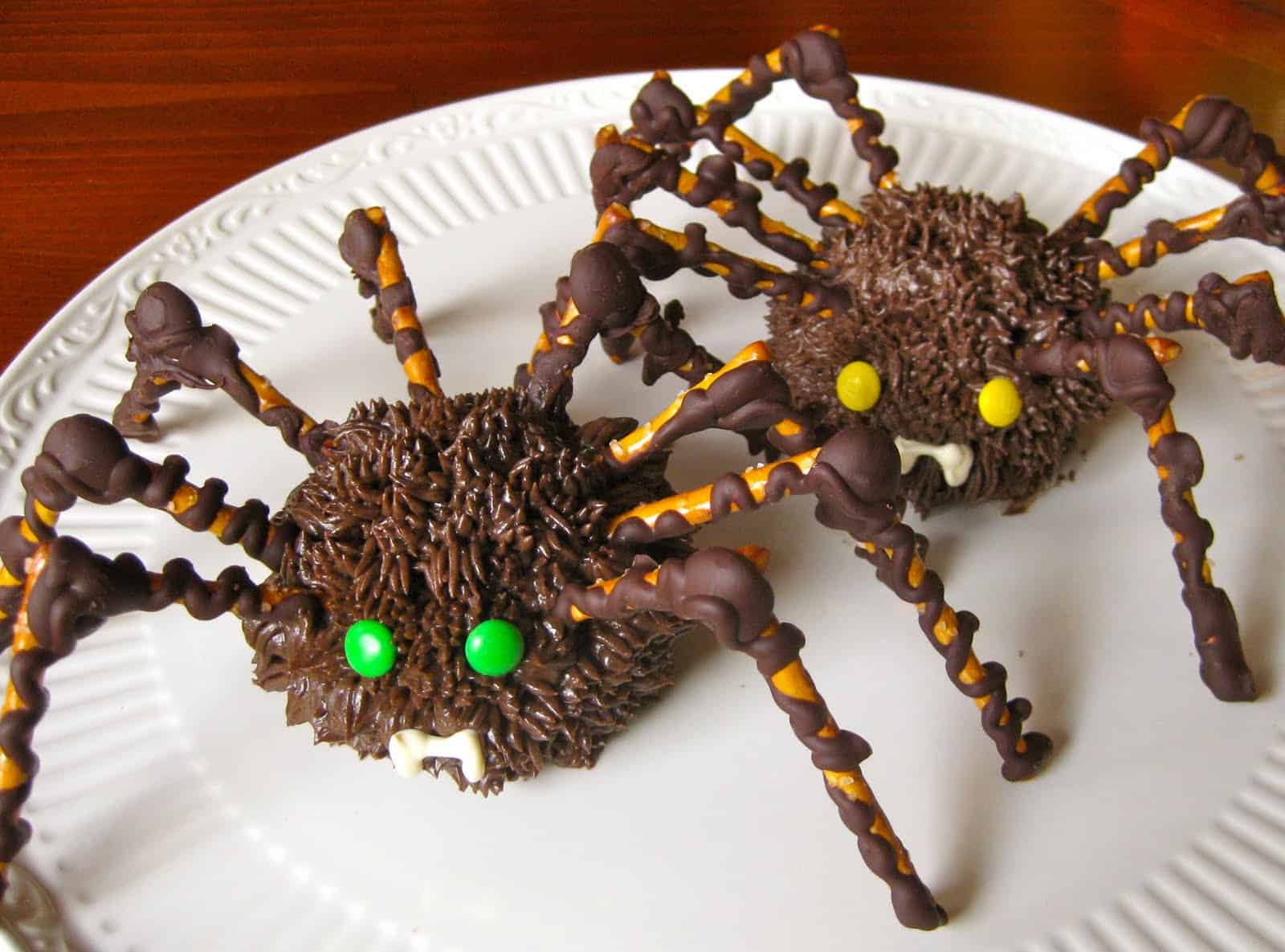 Two Spider Cupcakes with pretzel stick legs displayed on a white plate.