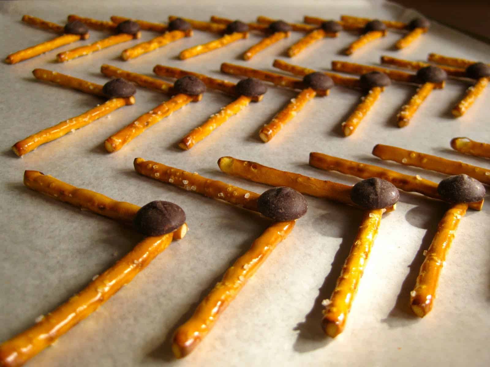 Stick pretzels with chocolate chips arranged on a baking sheet.